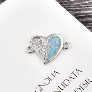 Macro detail of silver heart charm with white zircon pavé and blue opal gemstone