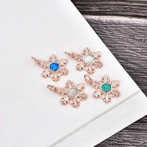 Rose gold snowflake pendants with colorful opal inlays on a dark wood background