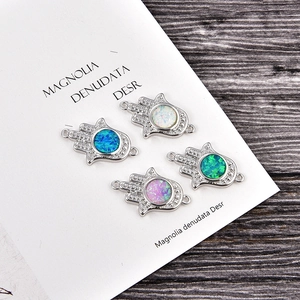 Hamsa Hand charms with opal and cubic zirconia stones on dark wood background