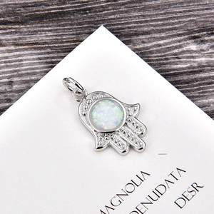 Macro shot of silver Hamsa Hand pendant with a central round opal inlay on wood surface