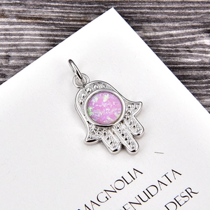 Macro detail of silver Hamsa Hand pendant with pink opal stone on wooden desk