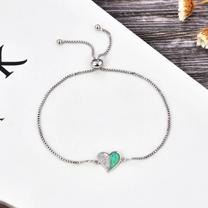 Detail of adjustable heart bracelet with white zircon and green opal on a wooden background