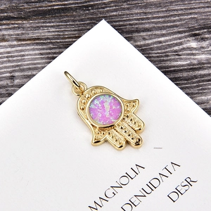 Macro shot of gold Hamsa Hand pendant with purple opal inlay on a white card