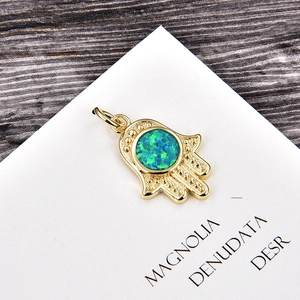 Detailed view of golden Hamsa hand pendant with green synthetic opal and beaded texture