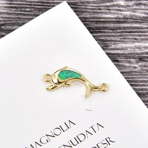 Macro detail of dolphin jewelry link with green opal stones and gold plating