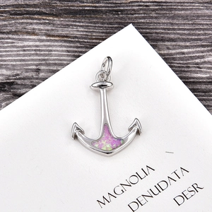 Macro detail of a silver anchor pendant with pink opal inlay on a rustic wooden background
