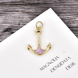 Macro detail of a gold-plated anchor pendant with pink opal inlay and hanging ring
