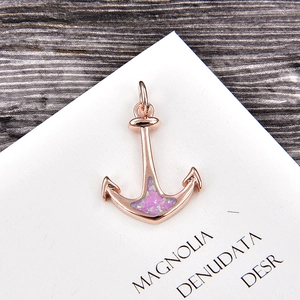 Detailed view of rose gold anchor pendant with iridescent pink opal center on wood background