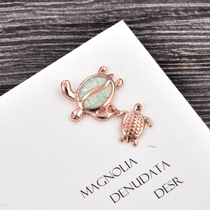 Detailed close-up of rose gold turtle charm with opal inlay on white display card