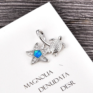 Macro shot of silver turtle and starfish pendant with blue opal inlay on white card