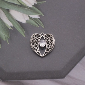 Detailed view of silver heart pendant with intricate hollow pattern and clear zircon stone