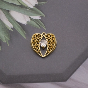 Close-up of golden hollow heart charm with clear crystal on a gray hexagonal display