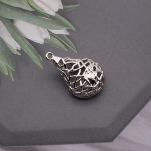 Detailed view of silver heart nest pearl cage pendant on dark stone background