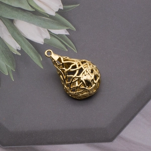 Detailed view of a gold hollow teardrop pendant on a modern hexagonal jewelry display