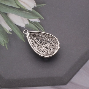 Detailed macro view of a silver teardrop hollow pendant with intricate woven mesh texture