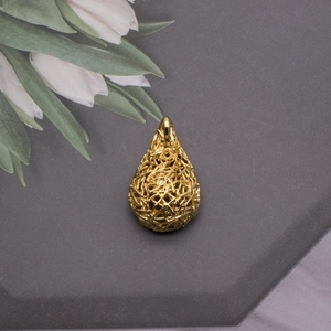 Close-up of golden teardrop hollow woven bird nest pendant with metallic texture