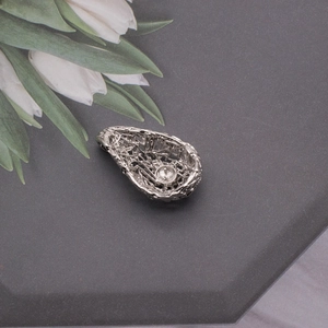 Detailed close-up of a silver hollow teardrop pendant with intricate woven texture and pearl