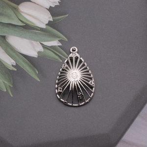 Detailed macro view of silver teardrop hollow pendant with sunburst pattern and floral relief