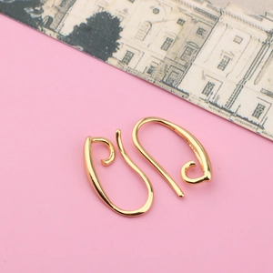 Macro shot of gold plated DIY ear hooks with elegant spiral lines on pink background