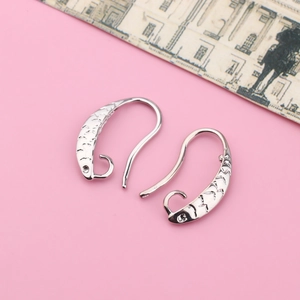 Detailed macro shot of silver fish-shaped earring hooks with textured scale patterns