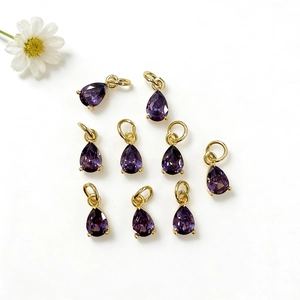 Dettaglio di nove ciondoli in zircone viola a goccia con anelli dorati per gioielli