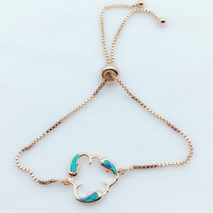 Detail of rose gold adjustable dolphin bracelet featuring blue opal inlay dolphin charms
