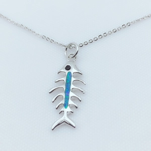 Macro detail of silver fish bone pendant featuring opal inlay and black gemstone eye