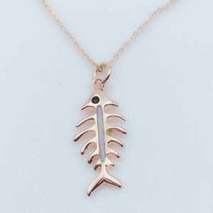 Close-up of rose gold fishbone pendant with opal inlay and black stone eye on chain