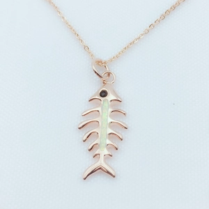 Close-up of rose gold fish bone pendant featuring opal inlay and tiny black zircon eye