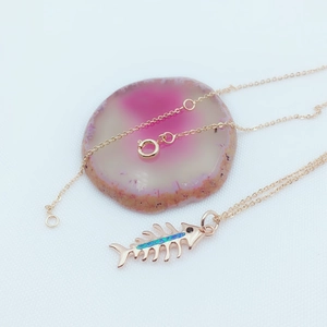 Detailed close-up of a 14k gold-plated fishbone pendant with blue opal on agate stone