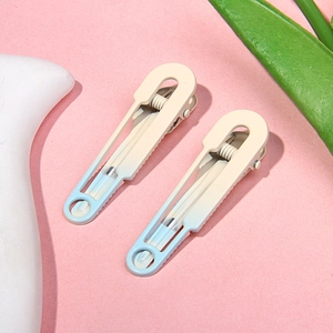 Macro detail of macabre beige and light blue gradient metal hair pins on pink surface
