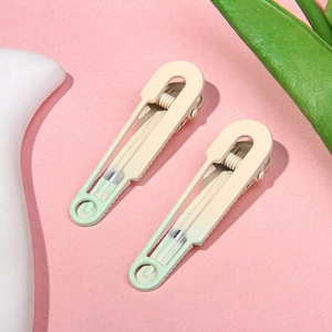 Detail view of two gradient cream and green matte metal hair clips on a pink background