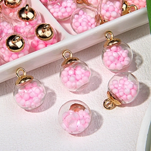 Nahaufnahme von Glaskugel-Anhängern mit rosa Perlenfüllung und Goldkappe für DIY-Schmuck