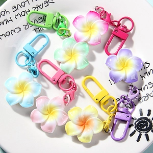 Macro detail of frangipani flower keychains in pastel colors on a white ceramic plate