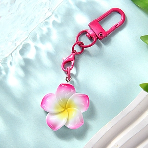 Close-up of pink gradient frangipani keychain with metallic D-ring on blue water base