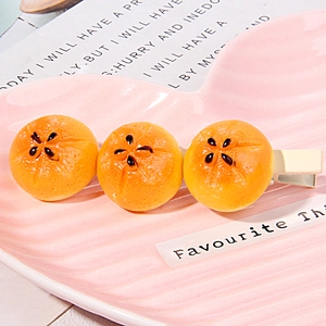 Detail of cute simulated resin orange slices on a metal hair clip in a pink heart tray
