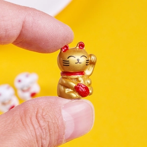 Macro shot of a mini golden resin lucky cat figurine held between fingers for scale