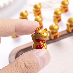 Miniature golden Maneki Neko resin figurine held at fingertip for micro landscape decor
