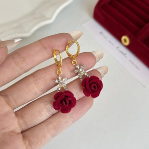 Detail of red velvet rose earrings with gold metal star and white crystal accents