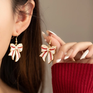 Detail of baseball theme bow earrings with red stitching on white enamel and gold base