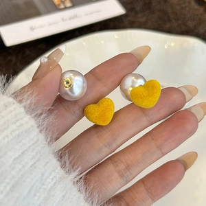 Yellow flocked heart earrings with large white pearls shown in a handheld close-up view
