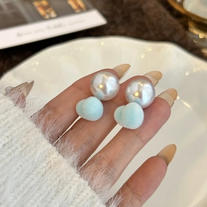 Detailed view of hand-held pearl earrings with blue heart-shaped flocked charms
