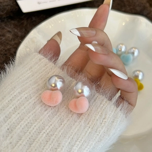 Close-up of pink flocked heart earrings with large white pearls held by hand