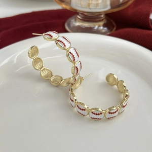 Close-up of C-shaped earrings with baseball stitching pattern on white enamel and gold metal