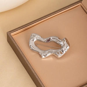 Broche irrégulière en métal liquide argenté poli dans un coffret à bijoux doré