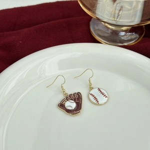 Macro detail of asymmetric baseball glove earrings on white porcelain and red fabric