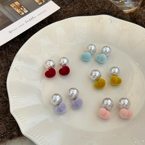 Detailed view of colorful velvet heart earrings and pearls in a white ceramic dish