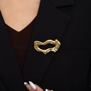 Broche dorée irrégulière effet lave polie miroir portée sur le revers d'un costume noir