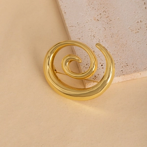 Élégante broche spirale dorée en métal poli présentée sur un support en pierre texturée
