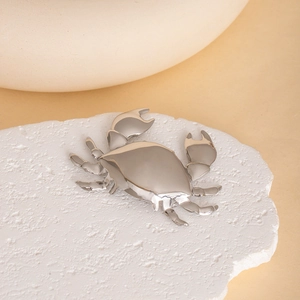 Polished silver crab brooch with mirror finish on white stone background